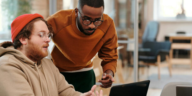 Two male coworkers huddling over a laptop to discuss their best fundraising tips