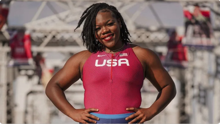 A smiling athlete in a red USA uniform, standing with hands on hips and looking confidently at the camera.