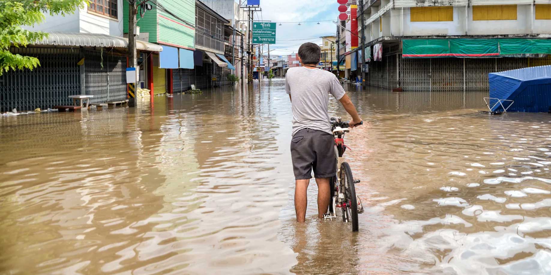 Man walking through a flooded street with his bicycle
