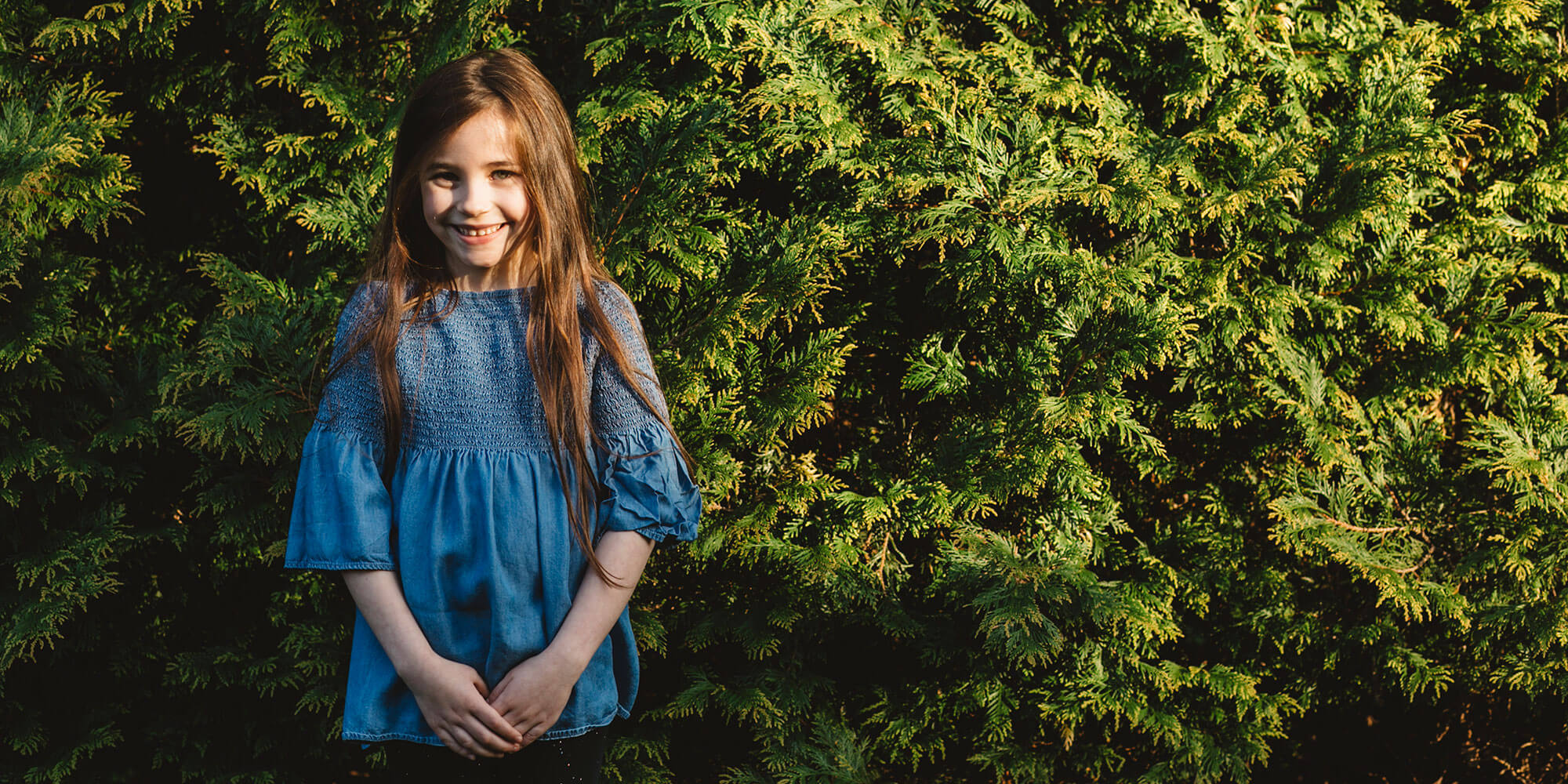 Little girl standing in front of shrubs
