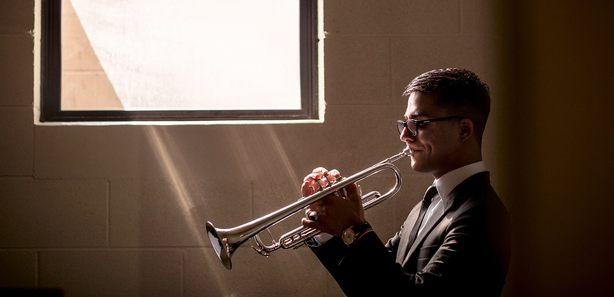 Man playing a trumpet by a window