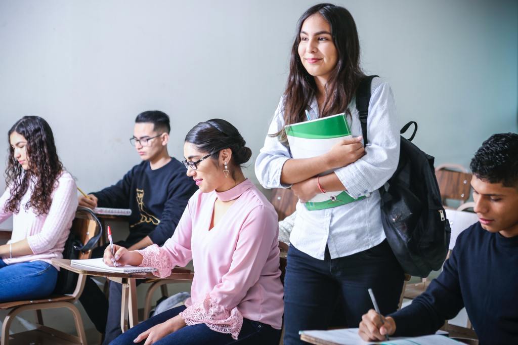 Female student standing in a classroom, holding a textbook