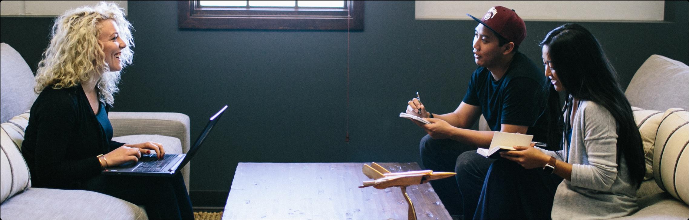 Woman working on a laptop and a man and another woman sitting in front of her taking notes